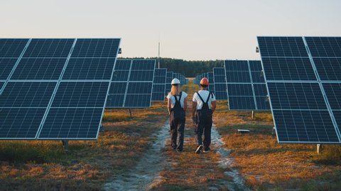 Business team of industrial technicians walking through solar park outside. Construction of concentrated solar power plant. Renewable energy. Ecology.