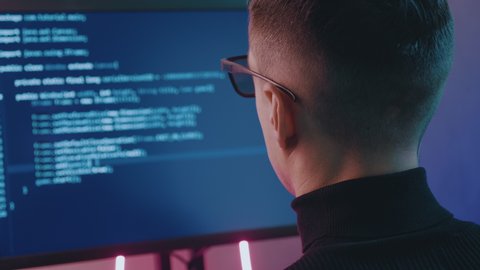 IT Professional Programmer man is typing code. Developer at work at computer. Hacker hacking late at night in neon lights.