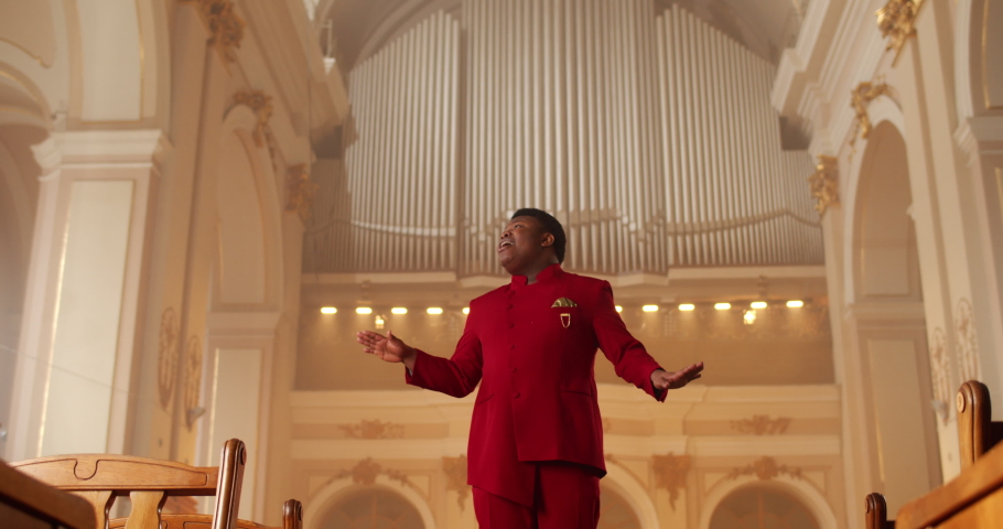 Emotional male singer performing worship music. Male Man wearing red suit moving hands while singing spiritual music in house of prayer. Concept of religion and people. Royalty-Free Stock Footage #1059629816
