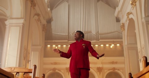 Emotional male singer performing worship music. Male Man wearing red suit moving hands while singing spiritual music in house of prayer. Concept of religion and people.