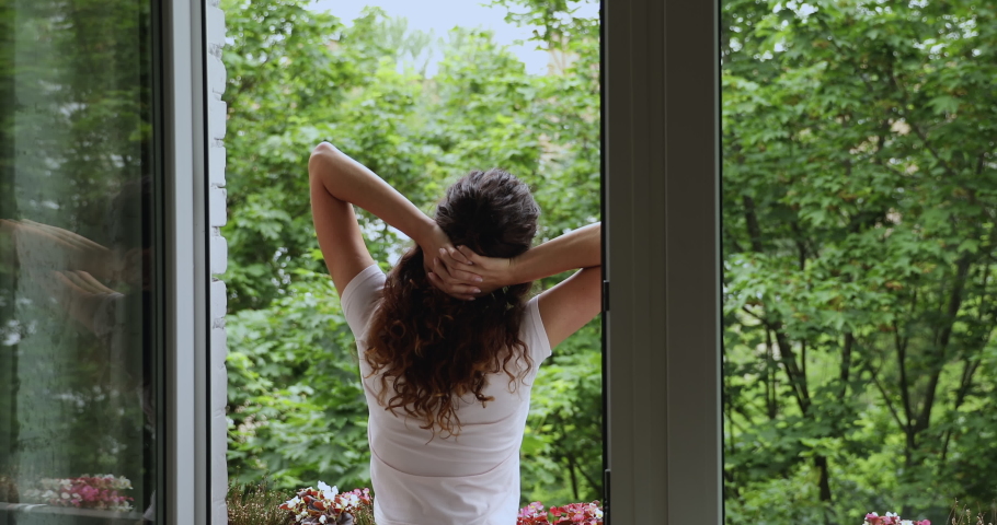 Rear back view serene awakened woman standing alone in summer terrace stretch neck muscles turn head to sides raise hands up feels refreshed enjoy morning admires summer nature view greeting new day Royalty-Free Stock Footage #1059629987