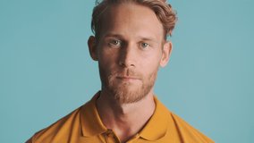 Handsome stylish blond man touching his beard confidently posing on camera over colorful background