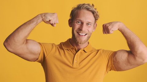 Attractive strong blond bearded guy happily showing biceps muscles on camera over colorful background. Power expression