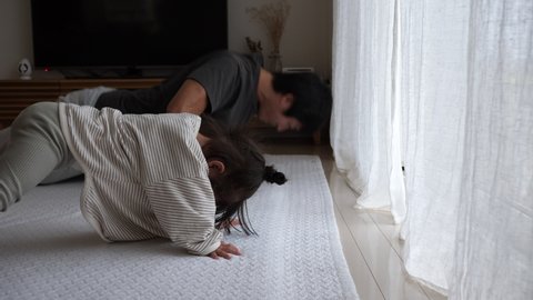 Asian little girl and his dad doing sport near the window at home at the cloudy daytime. Daughter trying to imitate push-ups next to her father. Home fitness and workouts - Βίντεο στοκ