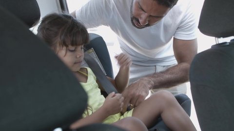 Father helping little girl to fastening child seat belts in car. Side view. Parenting or road safety concept