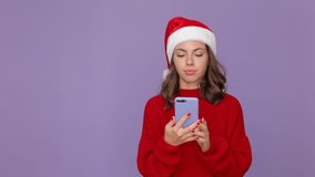 Young woman 20s in red knitted cozy sweater Santa Christmas hat using mobile cell phone doing selfie videoconference isolated on purple violet background studio. Happy New Year merry holiday concept