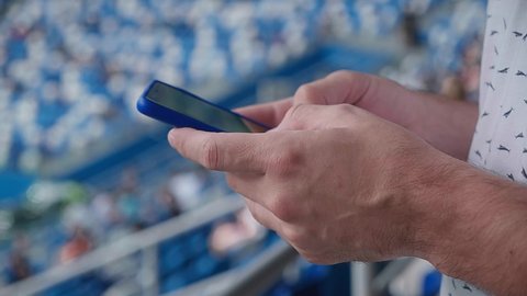 A young man writing a message on his phone during a match at the stadium. Mass event during coronavirus quarantine. Close-up of hands. High quality 4k footage