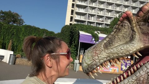 Kherson, Ukraine - 8th of September 2020: 4K At the Jurassic Park - Woman quarrels and spanks dinosaur

