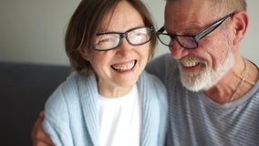 Happy elderly couple in love. Old man whispering secret to his wife. Gray-haired man and woman are sitting indoors on the sofa. Woman wears glasses and laughs cheerfully - Powered by Shutterstock - Get 15% off with code: PIKWIZARD15