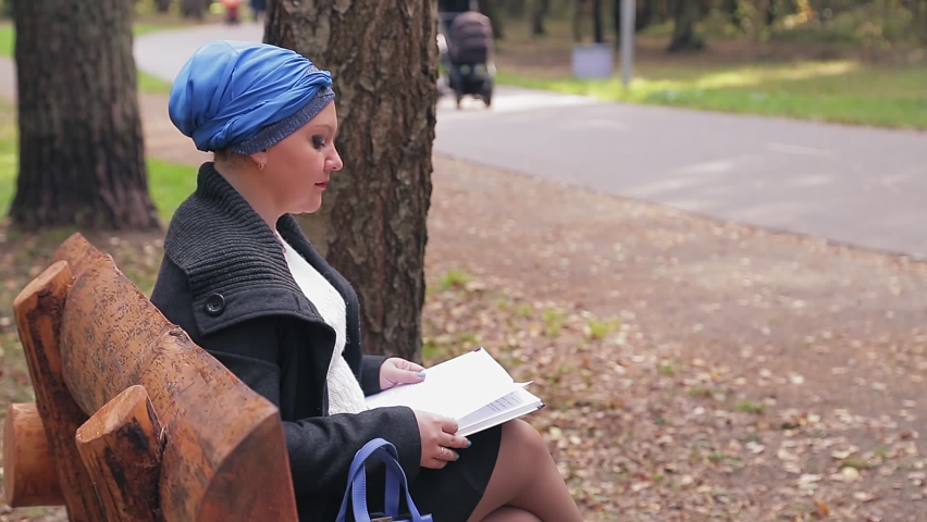 A Jewish woman in a traditional blue headdress in profile on a bench in the alley reads
