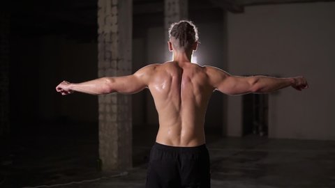 Strong bodybuilder posing backside after training with spotlight lens flare - showing his body and muscles spreading the hands
