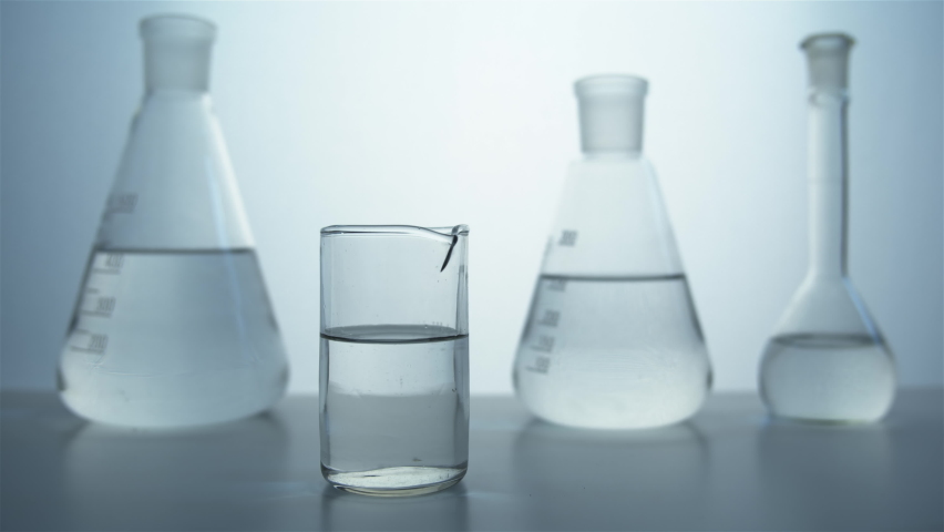 Close-up of a pipette in hand and a glass beaker against the background of flasks in the laboratory. A colorless liquid drips into a glass. Perfumery production. Royalty-Free Stock Footage #1059648272