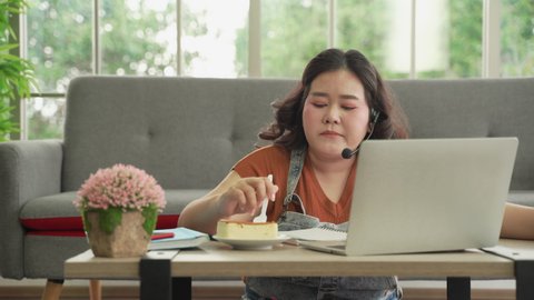 Asian plus size woman in casual eating working online with laptop computer online at home, eating unhygienic food
