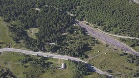 Aerial view of the ruralroad and forest in summer. Clip. Top view of beautiful summer mountains valley with growing pine trees and a driving car.