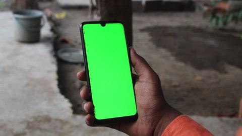 Closeup shot of hand holding mobile with green screen in a rural setting in India
