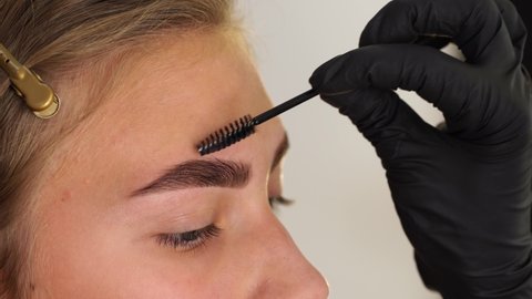 Professional styling, correction and lamination procedures of girl eyebrows in a beauty salon. Closeup view of client face and stylist's hands working in black gloves.