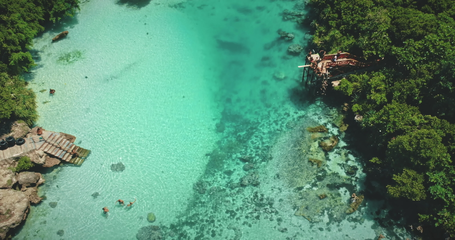 Tropical resort with emerald salt water lake of Weekuri, Indonesia, Asia. People recreation and swimming in saltwater lagoon at green tropic forest and grass. Cinematic rise up aerial view