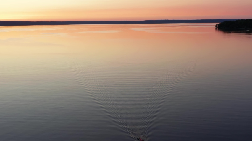 Sunset kayaking on a lake. Aerial drone view of young man kayaker on water with yellow orange purple pink night light at horizon. Sport activity out in the wild nature on calm summer evening. Sweden