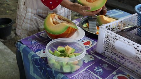 NAKHON PATHOM, THAILAND - SEPTEMBER 27: An unidentified woman cutting honeydew melon (cucumis melo) slices in plastic tray for sell to customers on September 27, 2020 in Nakhon Pathom, Thailand.