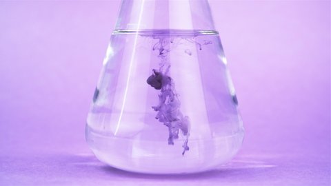 Glass flask with transparent liquid and blue substance on a pink background. Mixing liquids. Preparation of liquor medicine. Perfumery production.