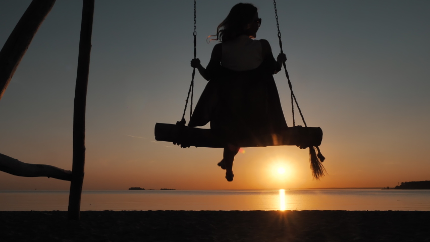 Silhouette of Young Happy Girl Swaying on Rope Swings Near Amazing Beach of Paradise Island at Sunset Alone Outdoors. Carefree Evening Relax on Resort, Free Calm Vacation on Beautiful Serene Sea Shore