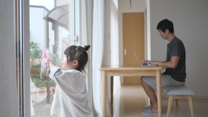 Mischievous kid drawing scribble on the glass window with crayon in the asian father working background. Remote work in the messy room. Busy childcare and parenting Royalty-Free Stock Footage #1059665954
