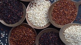 White, red and black quinoa seeds in spoon and on background rotating, close up, top view