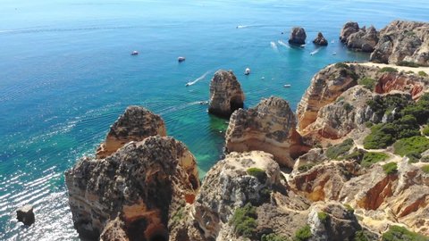 Drone aerial video of the Algarve coast outside Lagos, Portugal. Steep cliffs and turquoise water. In the distance Ponta da Piedade. Footage taken 2020.