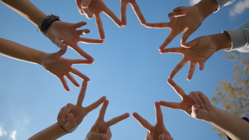 Bottom view of friends standing in circle doing symbol with fingers together over blue sky background. People doing circle with peace gesture with hands outdoors Royalty-Free Stock Footage #1059667910