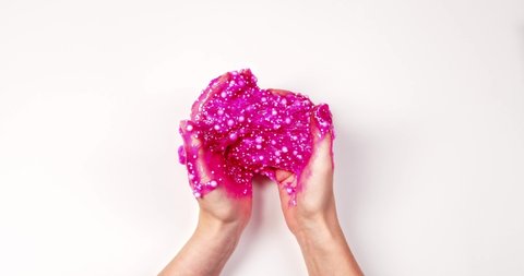 Playing with textured slime with bubbles, stretching the gooey substance for fun and stress relief. Close up and top view of female hand holding pink shining slime, squeezing it.