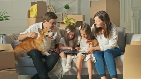 A Happy Family Uses a Tablet for Online Shopping, Sitting on the Couch at Home. Buying by the Internet. A Familly Sitting With a Cute Dog on the Couch at Home. Purchase Confirmation by the Internet