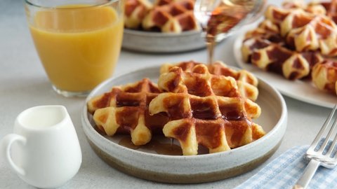 Pouring maple syrup on belgian waffles. Tasty breakfast waffles with sweet syrup and golden belgian waffles