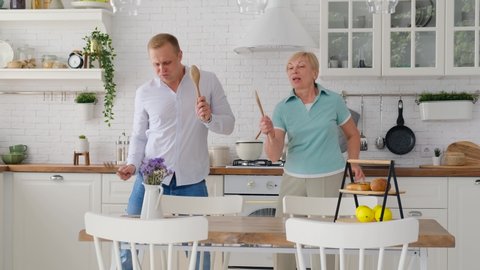 Adult son and elderly mother dancing and singing together in the kitchen