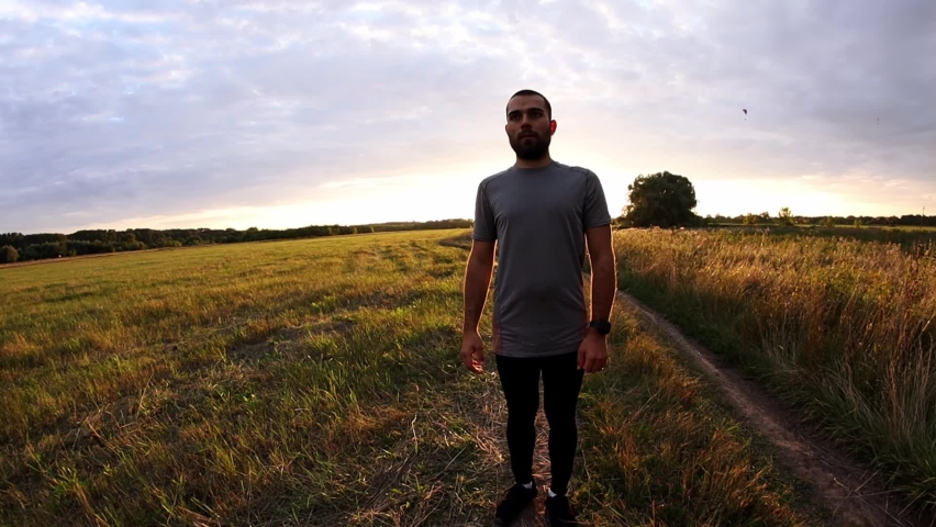 A MAN IN SPORTS CLOTHES STANDS AT SUNSET AND LOOKS AT THE WATCH