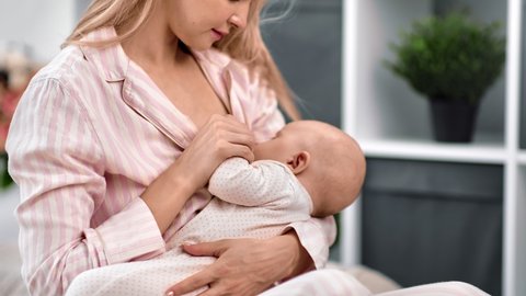 Caring mother feeding breast holding baby enjoying motherhood at cozy bedroom. Adorable woman during breastfeeding of cute toddler feeling love and tenderness. Medium close up shot on 4k RED camera