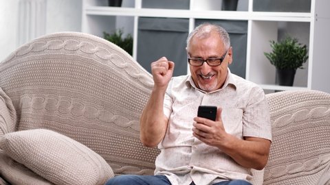 Joyful elderly 60s man excited look at screen of smartphone celebrating victory success or read good news. Overjoyed grandfather with phone happy to win mobile app sport bet. 4k Dragon RED camera