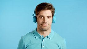 Handsome young man with trendy hairdo dancing with blue headphones in studio against bright background. Music, dance, radio concept, slow motion