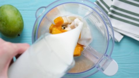 Pouring natural yogurt in blender to make a tropical banana mango smoothie or milkshake. Slow motion. Preparing healthy smoothie
