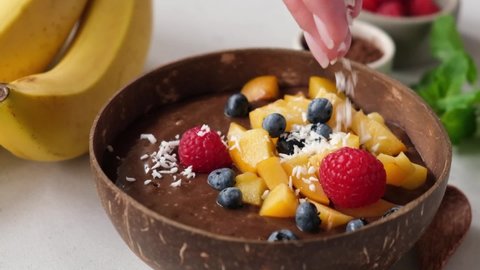 Decorating chocolate smoothie bowl with coconut flakes in slow motion. Healthy vegan vegetarian carob smoothie bowl