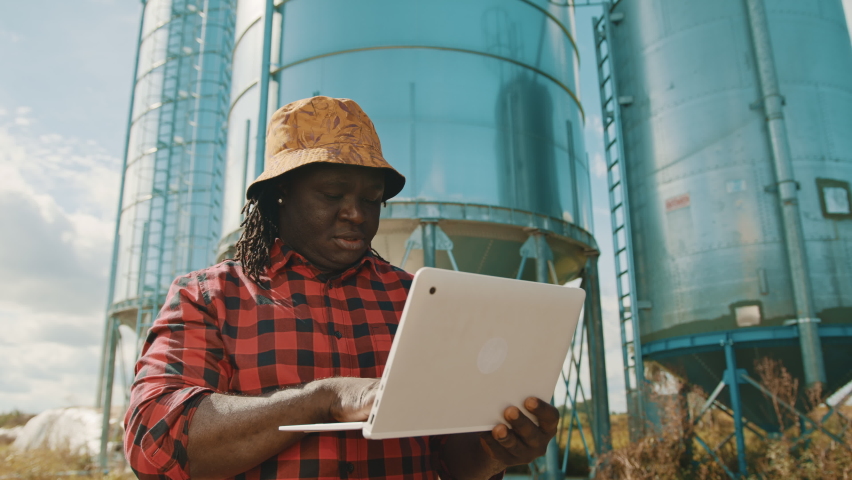 African farmer using laptop in front of the silo storage system. High quality 4k footage