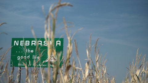 State of Nebraska welcome sign along the highway with corn fields during the day.
