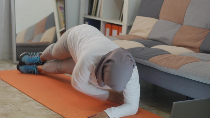 Asian muslim woman wearing hijab doing exercise at home while watching online video instruction on laptop, indoor home workout concept, keep healthy on new normal lifestyle, side plank twist | Shutterstock HD Video #1059696398