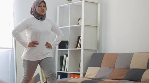 Asian muslim woman wearing hijab doing exercise at home while watching online video instruction on laptop, indoor home workout concept, keep healthy on new normal lifestyle, lunges 스톡 비디오