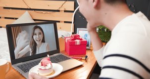back of asian young man has video chat online by laptop while celebrating birthday and giving cake for his girlfriend