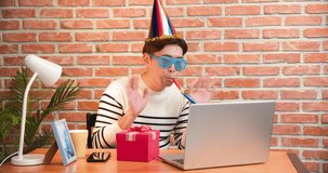 funny asian young man wearing birthday hat has video chat online by laptop while celebrating and giving present box for his friend