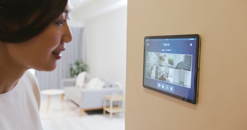 Asian girl use smart home app to watch surveillance system by touching the screen of tablet pc on wall
