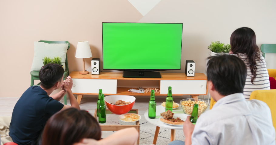 four asian friends are sitting on couch in living room and watching green chroma key screen TV while eating snacks and drinking beverage with nervous mood Royalty-Free Stock Footage #1059697004