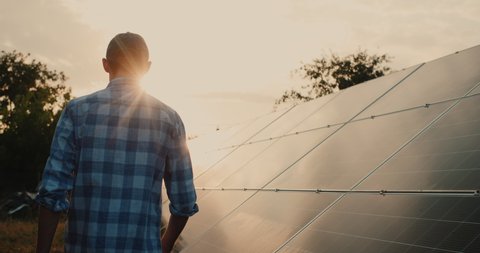 The owner walks along the panels of the terrestrial solar power plant, the setting sun illuminates him