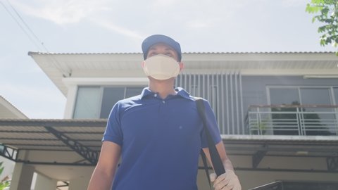 Low angle shot with circle pan of Asian delivery man in blue uniform with face mask carrying bag of food delivering food to customer home during covid virus pandemic. He standing outdoor in village.