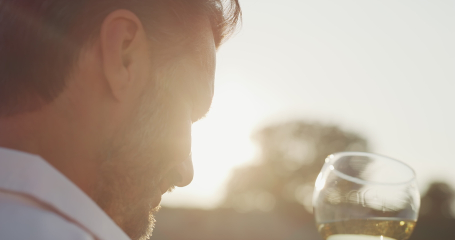 Authentic shot of happy handsome elegantly dressed man is tasting a flavor and drinking fresh white wine poured in transparent glass on scenic vineyards background at sunset. Royalty-Free Stock Footage #1059709436
